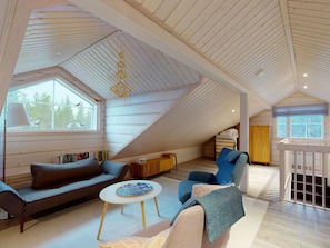 A spacious loft with a sloped ceiling, a sofa, a chair, a small table, and a bookshelf.