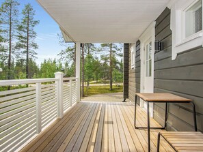 A wooden deck with a white railing, a table, and chairs, leading to a house with a grey exterior.