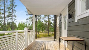 Eine Holzterrasse mit weißer Geländer, einem Tisch und Blick auf ein bewaldetes Gebiet.