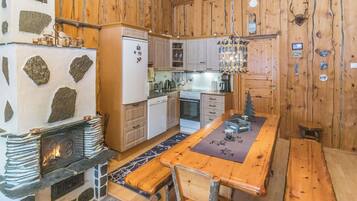 A rustic kitchen with wooden walls, a stone fireplace, and a dining area with a wooden table.