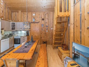 A rustic cabin interior with a wooden dining table, kitchen area, and a staircase. - Aihki 1 by Interhome (Inari)