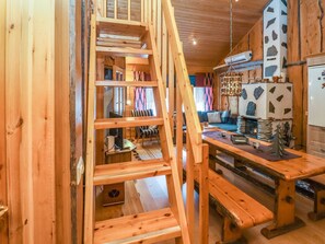 Interior de madera con escalera de madera, zona de comedor con bancos y área de cocina con refrigerador y objetos decorativos.