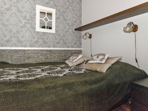 Un dormitorio con pared de ladrillo, ventana con diseño geométrico y cama con ropa de cama estampada.