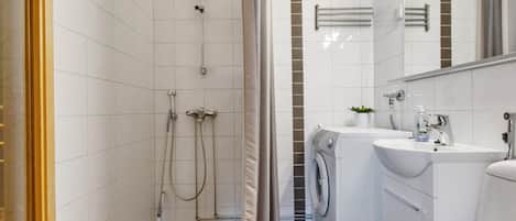 A bathroom with a shower, a washing machine, and a sink.
