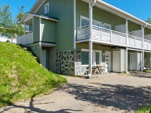 Ein zweistöckiges Gebäude mit grüner Fassade, steinernen Verkleidungen und einer überdachten Außenbereich-Sitzgelegenheit.