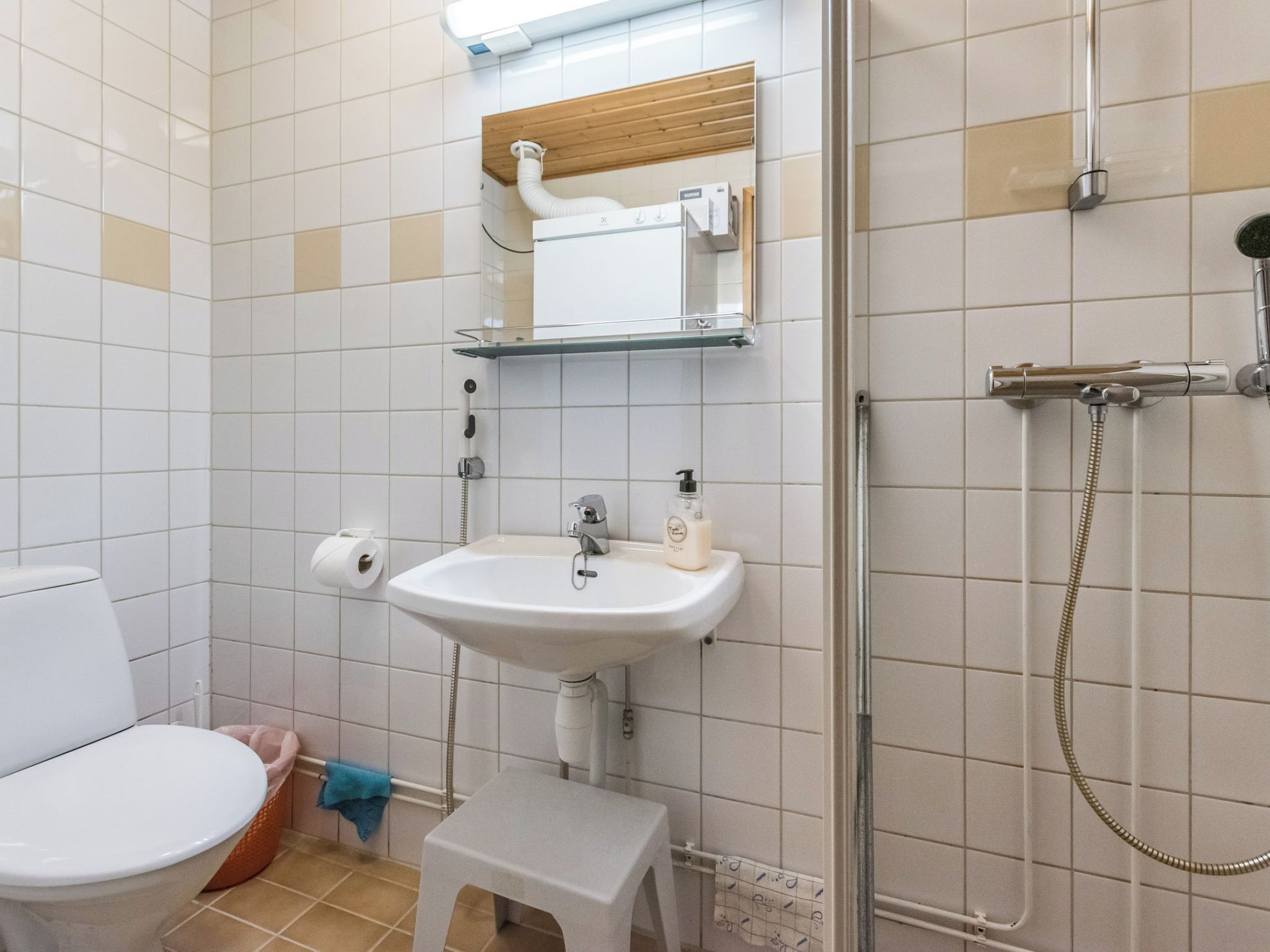 A bathroom with a toilet, sink, shower, and a small stool.