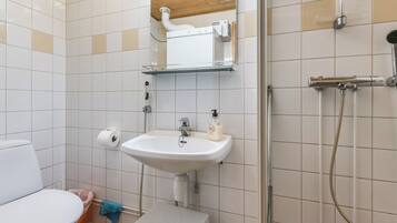 A bathroom with a toilet, sink, shower, and a small stool.
