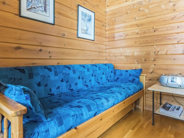L’intérieur d’un chalet en bois, avec un canapé bleu à motifs, des murs en bois et une table sur laquelle se trouve une radio.