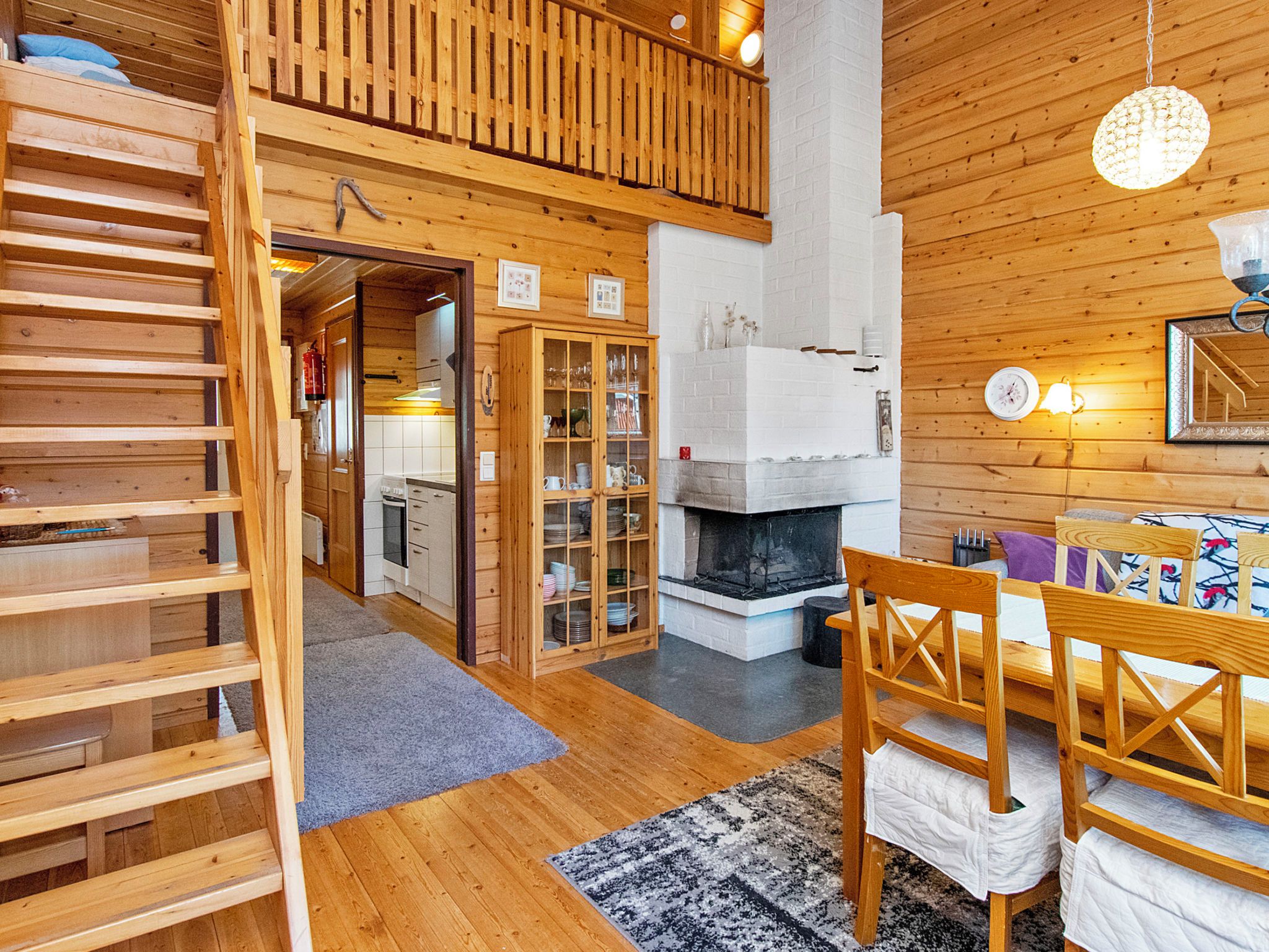 A wooden interior with a fireplace, a dining area with chairs, and a staircase leading to an upper level.