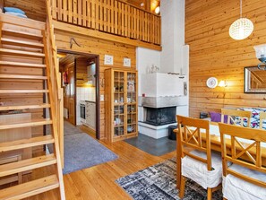 A wooden interior with a fireplace, a dining area with chairs, and a staircase leading to an upper level.