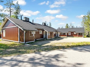 A row of wooden cabins with pitched roofs, a gravel driveway, and surrounding trees. - Hirvasaho a 2 by Interhome (Inari)
