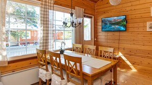 Un interior de madera con una mesa de comedor, sillas, una lámpara de araña, un televisor y ventanas amplias.