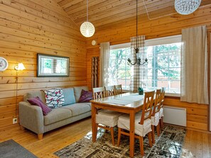 Interior acogedor de una cabaña con una mesa de comedor de madera, sillas, un sofá y un amplio ventanal con cortinas.