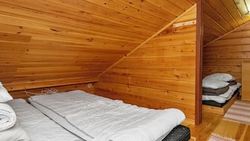 Habitación de cabaña de madera con una cama individual, techo de madera y un pequeño espacio de almacenamiento con ropa de cama doblada.