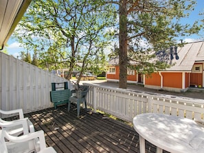 A wooden deck with outdoor furniture, a tree, and a building in the background.