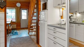 Cocina compacta con armarios blancos, un refrigerador y un microondas. Una escalera de madera conduce a un comedor con una mesa y sillas.