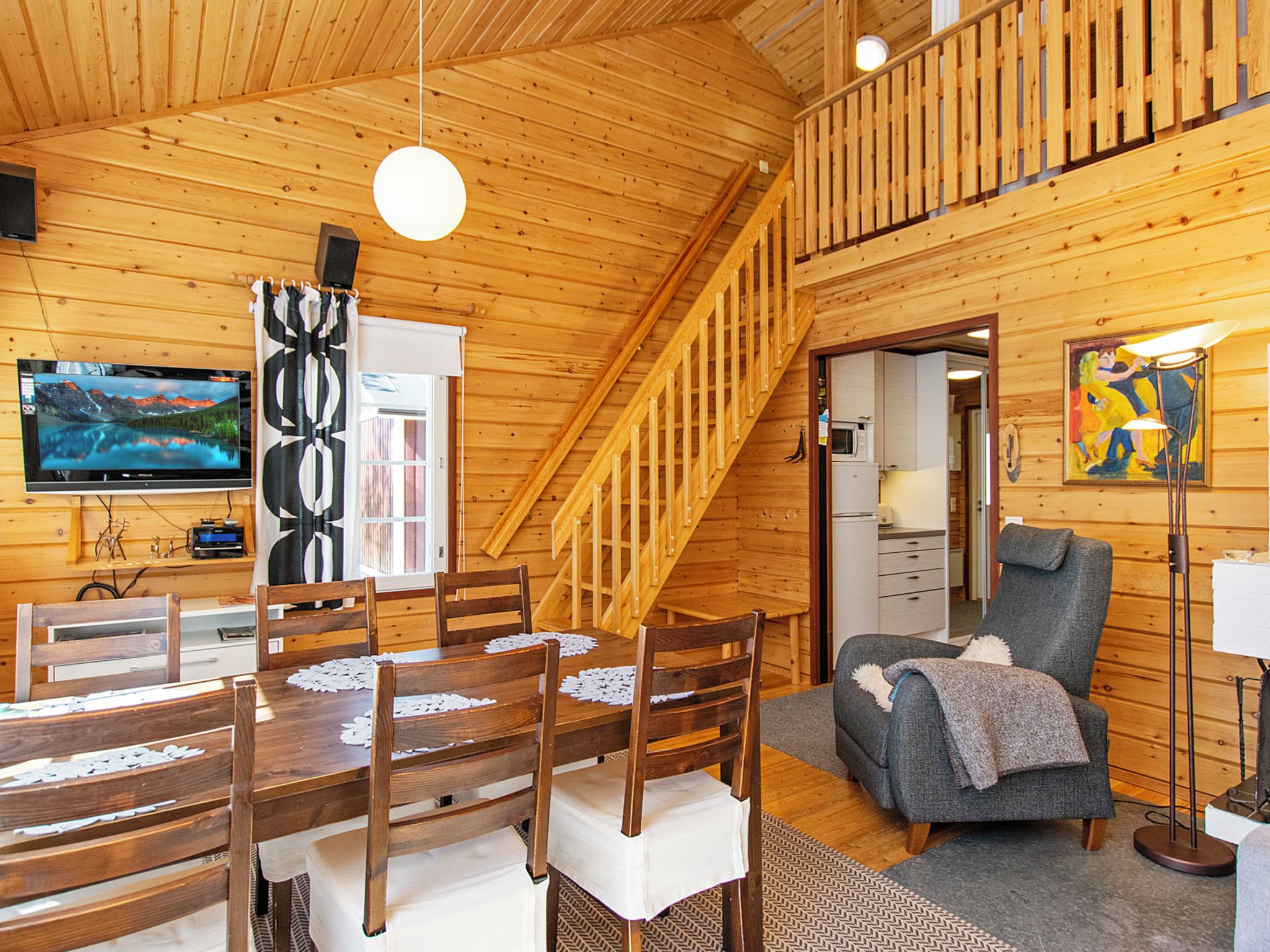 A wooden cabin interior with a dining area, a staircase, a living room, and a kitchen.