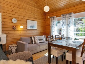 A cozy cabin interior with a wooden ceiling, a sofa, a dining table, and a window with curtains.
