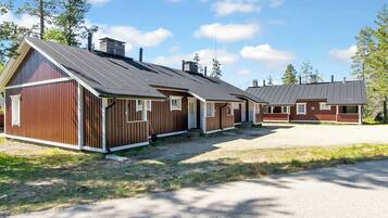 A row of wooden cabins with pitched roofs, a gravel driveway, and surrounding trees.
