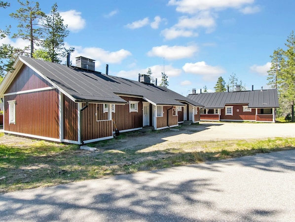 A row of wooden cabins with pitched roofs, a gravel driveway, and surrounding trees. - Hirvasaho a4 by Interhome (Inari)