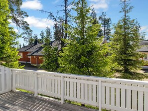 A wooden deck with a white railing, surrounded by trees and houses with red and white exteriors.