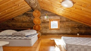 Un dormitorio acogedor en un ático con paredes de madera, techo inclinado, una ventana pequeña y dos colchones.