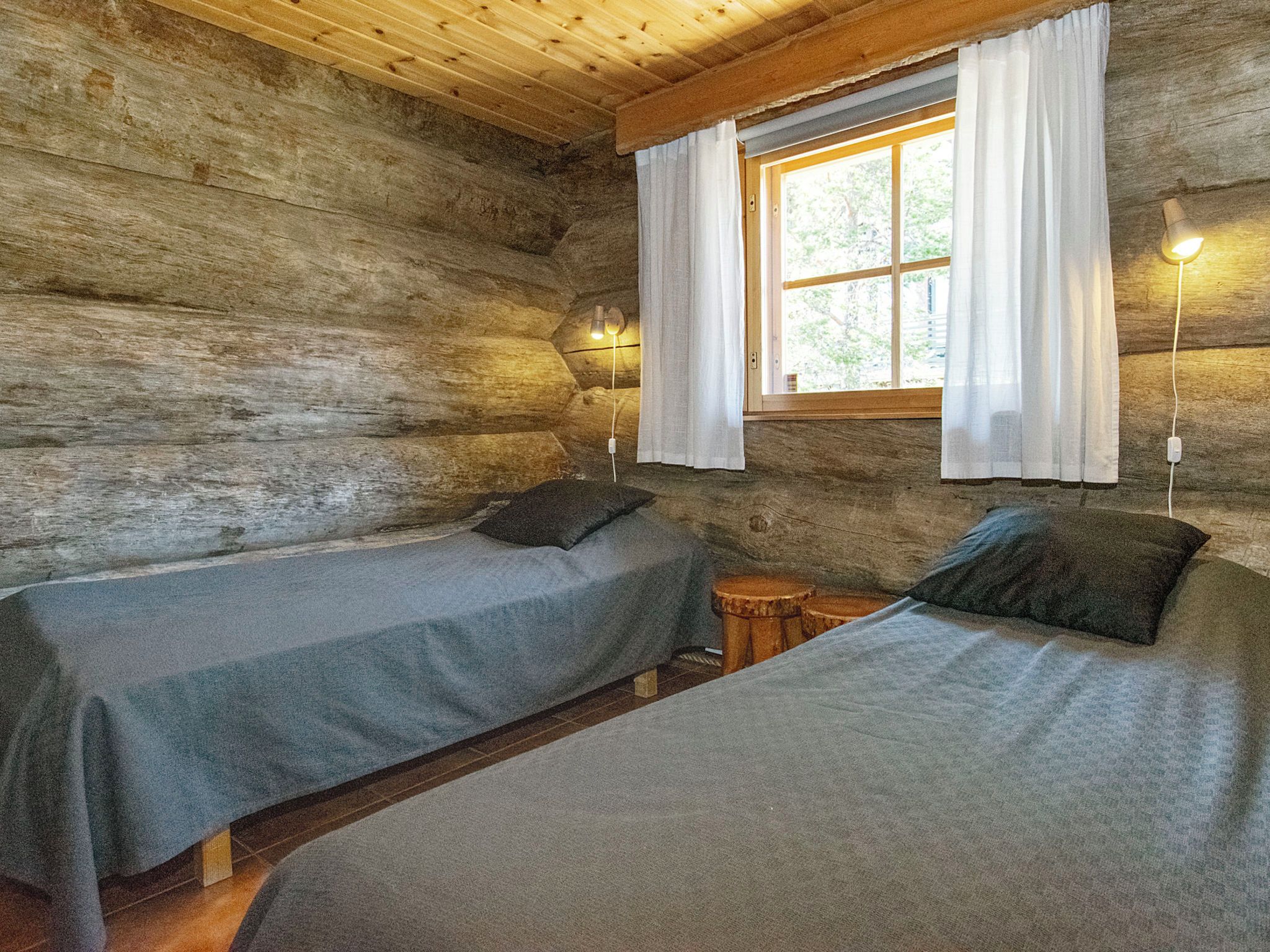 A cabin with two beds, a window with curtains, a wall-mounted lamp, and a small wooden stool.