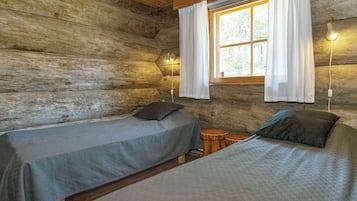 A cabin with two beds, a window with curtains, a wall-mounted lamp, and a small wooden stool.