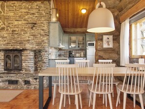A rustic kitchen with stone walls, wooden ceiling, and a dining area with white chairs and a table. - Kauniskelo a by Interhome (Inari)