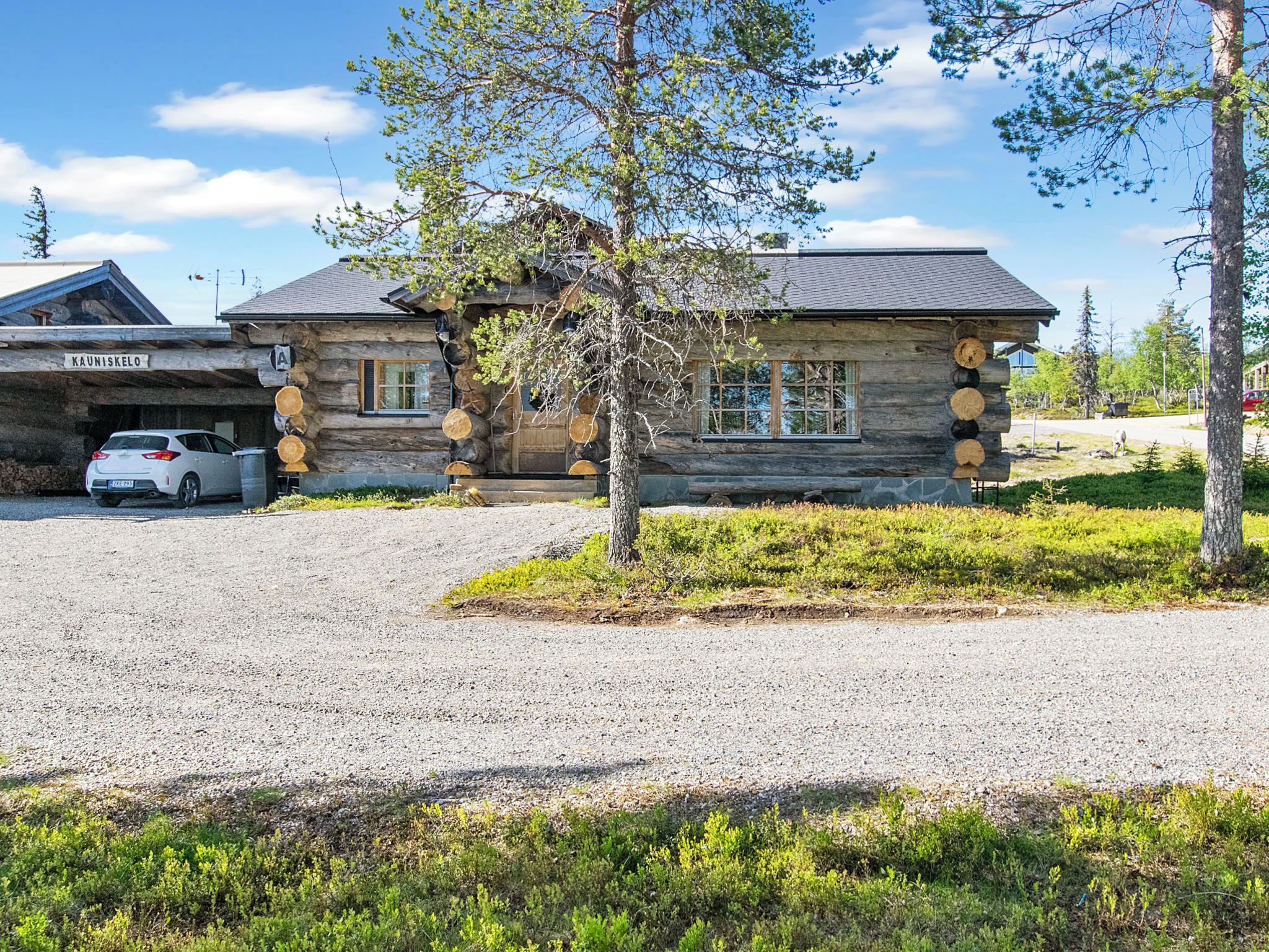 A log cabin with a gravel driveway and a car parked in the garage.