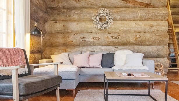 Interior acogedor de una cabaña de troncos con sofá, sillón y una pequeña mesa.