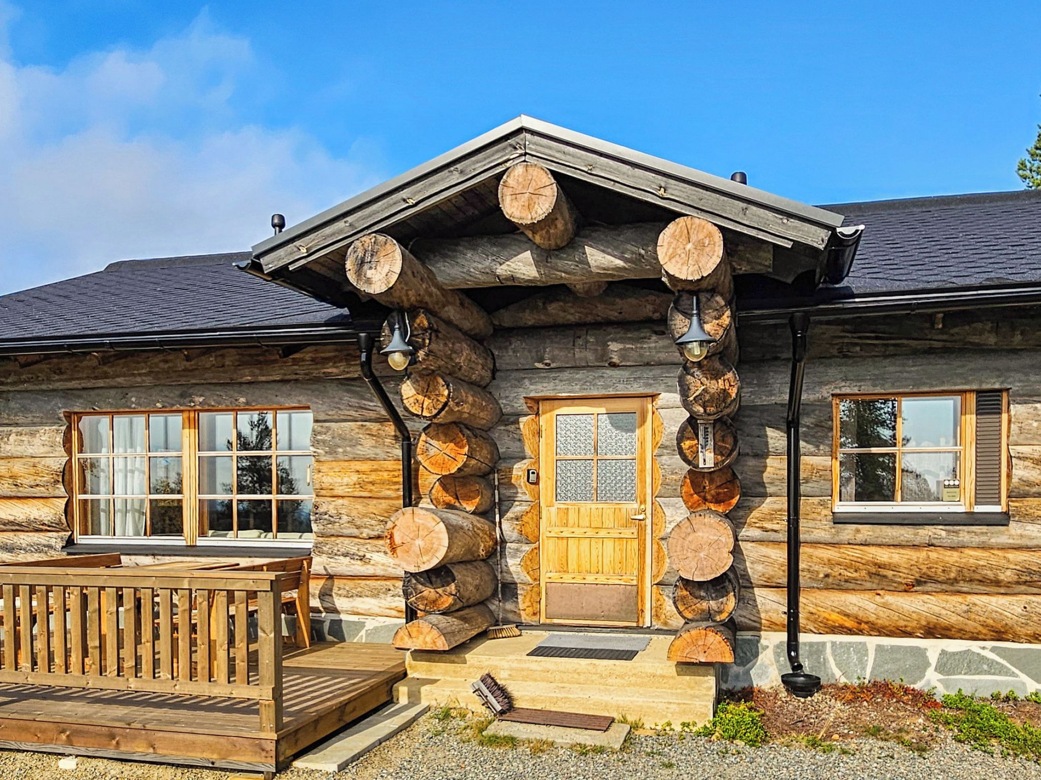 A log cabin with a wooden porch, a stone foundation, and a large wooden door.