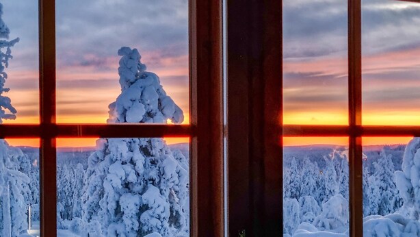 Uitzicht door een raam met een rasterpatroon, toont een besneeerd landschap met bomen en een zonsondergang.