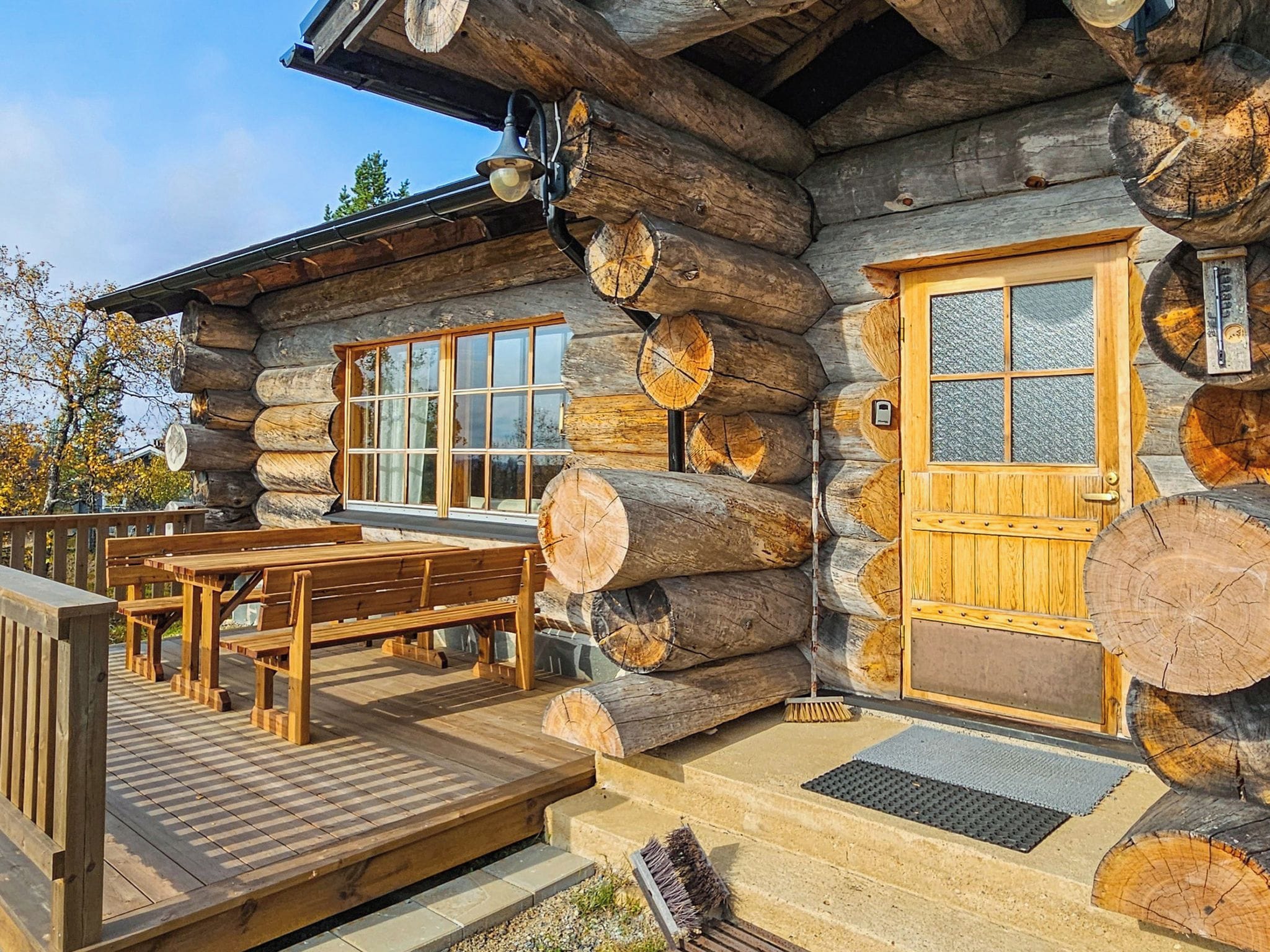 Une cabane en rondins avec une terrasse en bois, un banc et une porte.