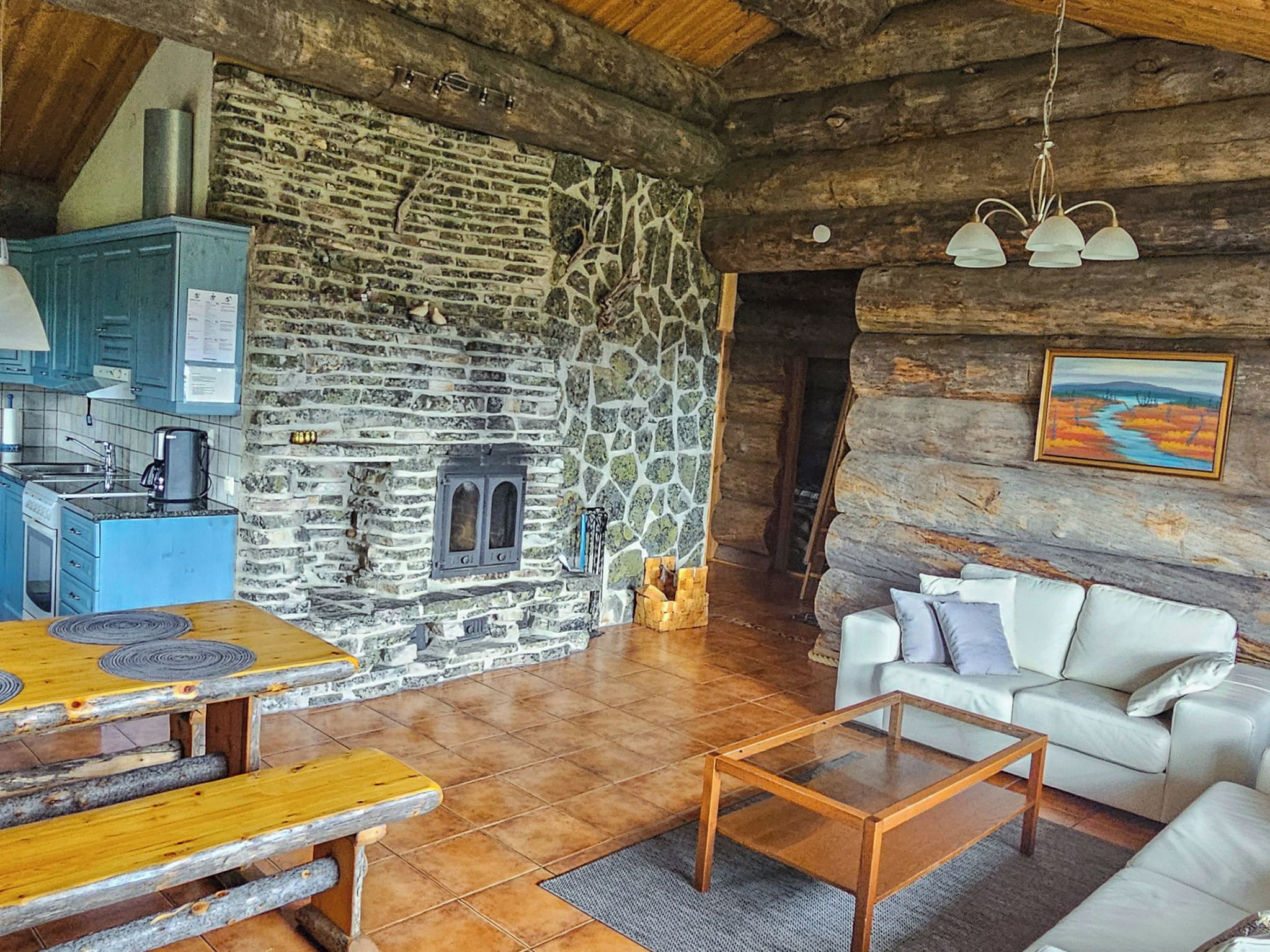 A rustic interior with a stone fireplace, a wooden dining table, a sofa, and a kitchen area.