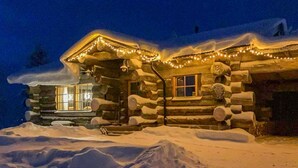 Een blokhut met een sneeuwbedekte dak, verlicht met lichtjes, omringd door sneeuw.