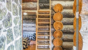 Het interieur van een blokhut, met een houten ladder die leidt naar een slaapkamer op een entresol, met een bedovertrek in ruitpatroon.