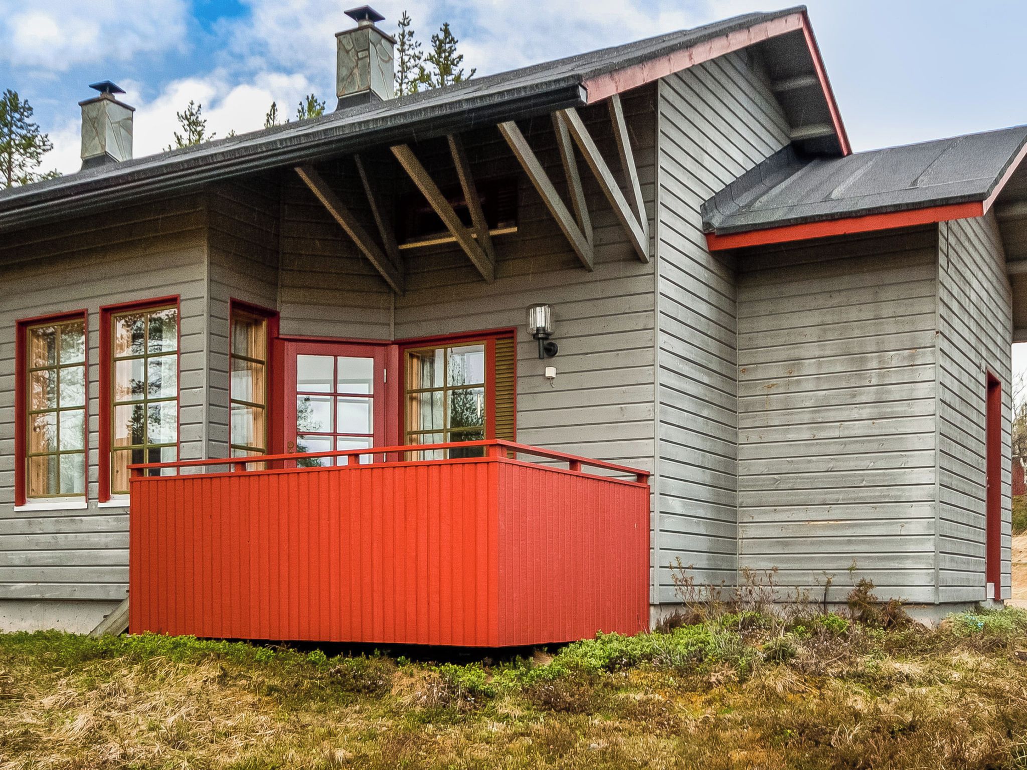 A house with a red balcony, grey siding, and a chimney.