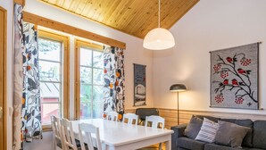 Una sala de estar moderna con una mesa de comedor blanca, un sofá gris y un ventanal con cortinas.