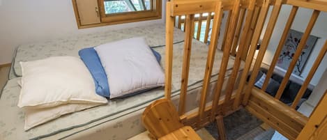 Una habitación con una cama, una silla de madera y un ventanal.