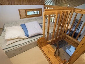 Une pièce avec un lit, une chaise en bois et une fenêtre.