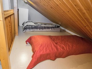 A room with a sloped ceiling, a red bed, and a white wall with a whiteboard.