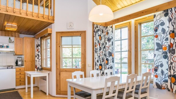 Una cocina moderna con armarios de madera, una encimera blanca y un comedor con una mesa y sillas blancas.