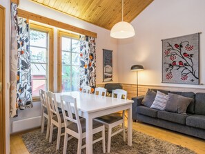 A modern living room with a dining area, wooden ceiling, and a large window with curtains.