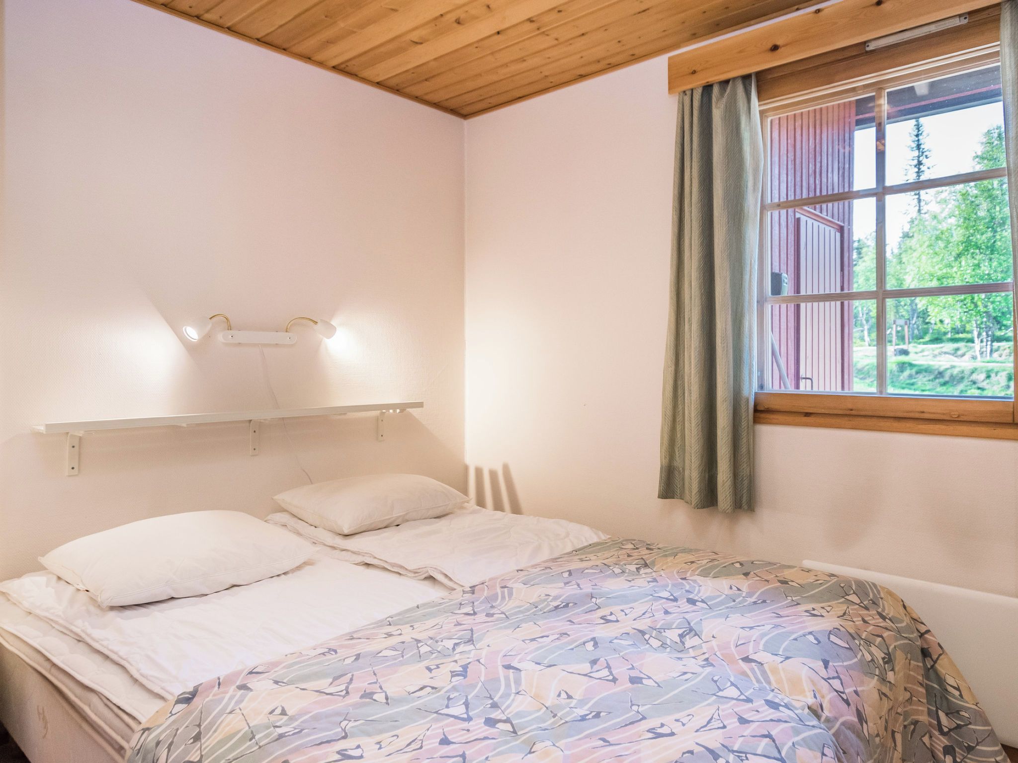 Un dormitorio con cama, cabecera, ventana con cortinas e iluminación en el techo.