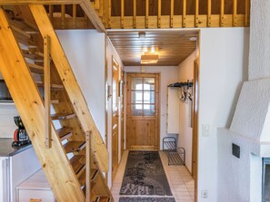 Un escalier en bois menant à un deuxième étage, un couloir avec une porte en bois, un petit coin salon et une cuisine équipée d’une machine à café.