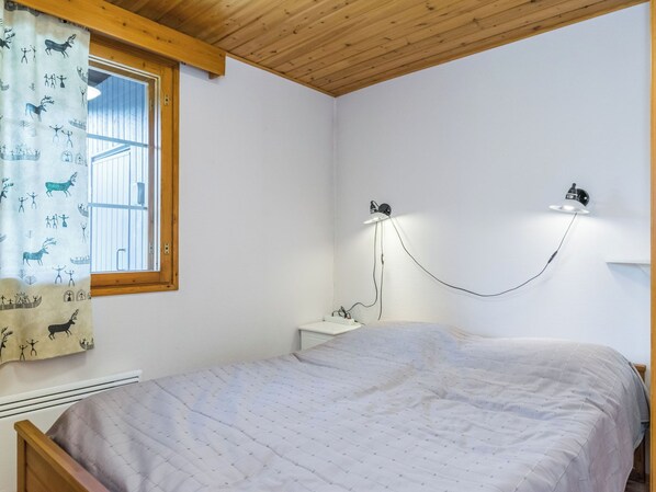 A bedroom with a bed, a window with curtains, a wall-mounted lamp, and a bedside table.