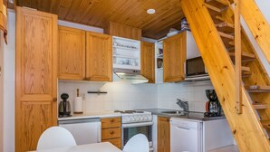 Cocina compacta con armarios de madera, encimera blanca, estufa, lavavajillas y una escalera de madera.