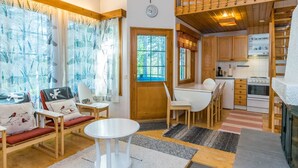 Una sala de estar acogedora y bien iluminada, con un sofá, sillas, una mesa redonda y una cocina con armarios de madera y una estufa.