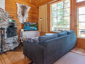 A cozy cabin interior with a stone fireplace, a television, and a large window offering a view of the outdoors.